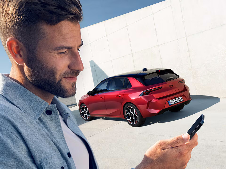 Uomo usa l'app Opel Connect al telefono con Opel Astra rossa sullo sfondo