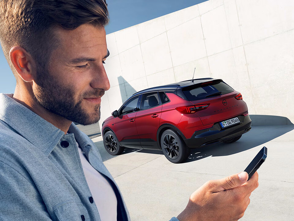 Un uomo accede all'app MyOpel tramite OpelConnect; alle spalle compare un Opel Grandland rosso