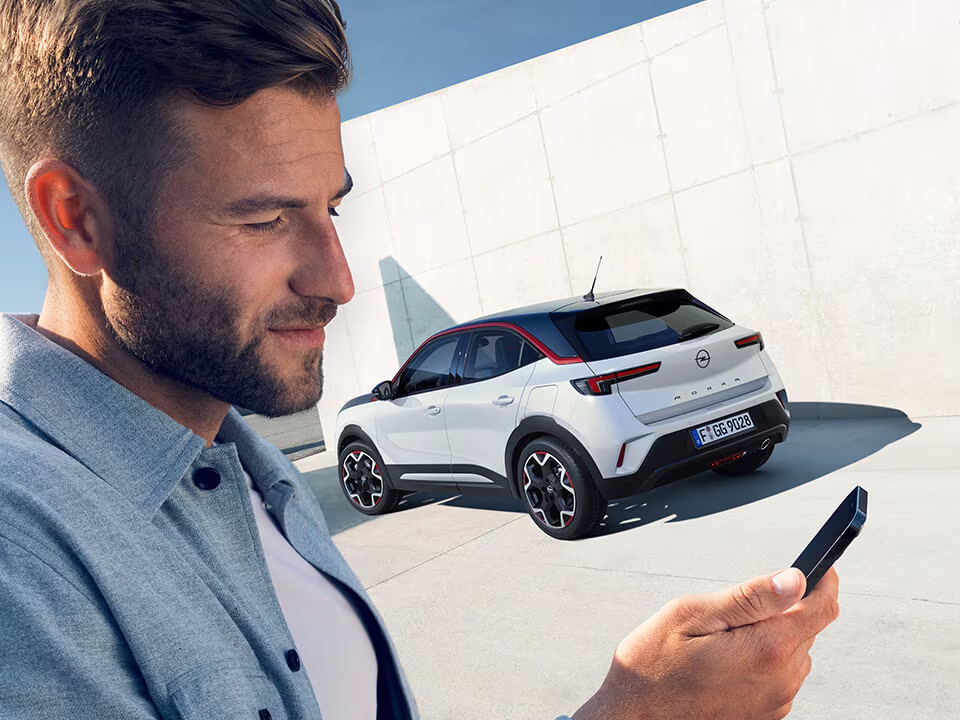 Uomo usa l'app Opel Connect sul telefono con Opel Mokka bianco sullo sfondo